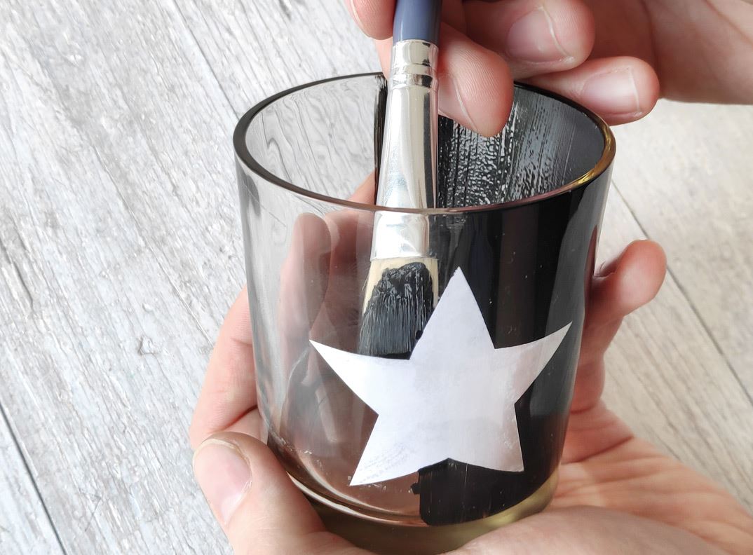 The inside of a glass is getting painted black with a brush.